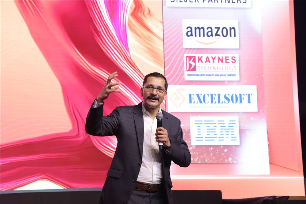 Chinmay speaking on a conference stage in front of sponsor logos